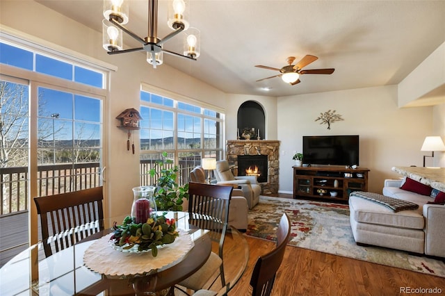 living area with a stone fireplace, wood finished floors, and ceiling fan with notable chandelier