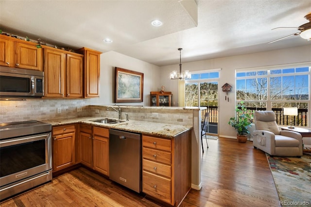 kitchen featuring brown cabinets, a sink, tasteful backsplash, stainless steel appliances, and a peninsula