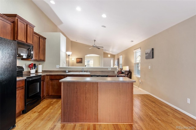 kitchen featuring lofted ceiling, a kitchen island, black appliances, sink, and light hardwood / wood-style flooring