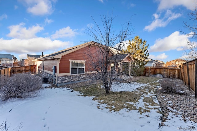 snow covered rear of property featuring central AC unit