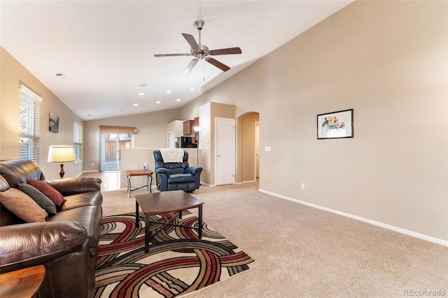 living room with a ceiling fan, light colored carpet, arched walkways, vaulted ceiling, and baseboards