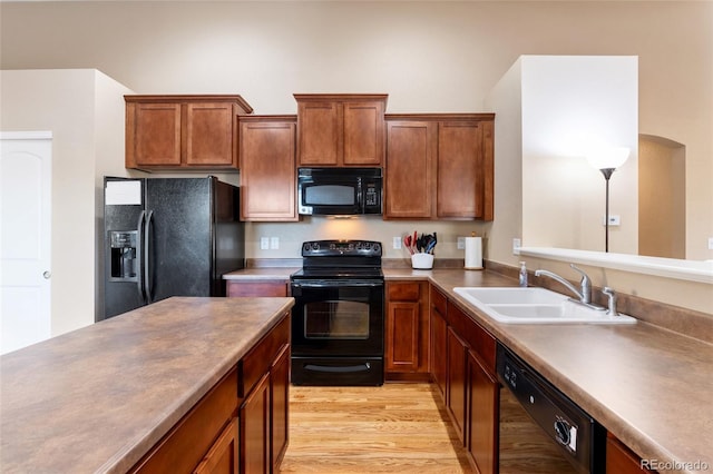 kitchen with a sink, brown cabinets, black appliances, and light wood finished floors