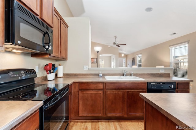 kitchen with brown cabinetry, a ceiling fan, vaulted ceiling, a sink, and black appliances