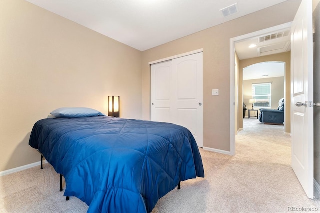 bedroom featuring light carpet, arched walkways, baseboards, visible vents, and a closet