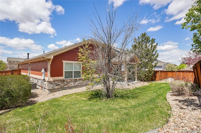 view of home's exterior featuring a yard, fence, central AC unit, and stone siding
