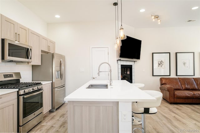 kitchen featuring sink, stainless steel appliances, tasteful backsplash, light brown cabinetry, and a center island with sink