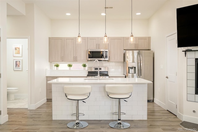 kitchen with a breakfast bar area, a kitchen island with sink, light brown cabinets, and stainless steel appliances