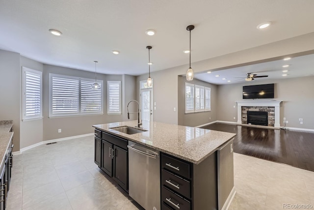 kitchen featuring a stone fireplace, dishwasher, sink, hanging light fixtures, and a kitchen island with sink