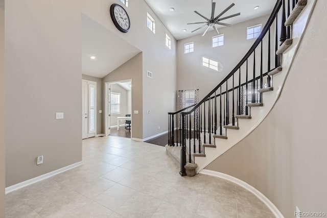 foyer entrance with ceiling fan, a towering ceiling, light tile patterned floors, and a wealth of natural light