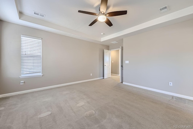 carpeted spare room featuring ceiling fan and a raised ceiling