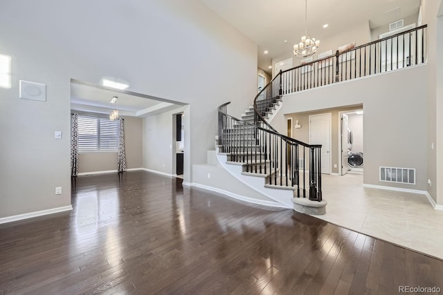 entrance foyer with a chandelier, hardwood / wood-style floors, a raised ceiling, and a high ceiling