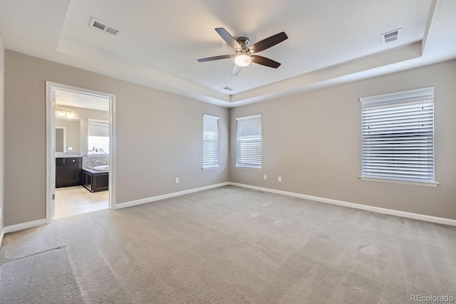 empty room featuring a tray ceiling, light colored carpet, and ceiling fan