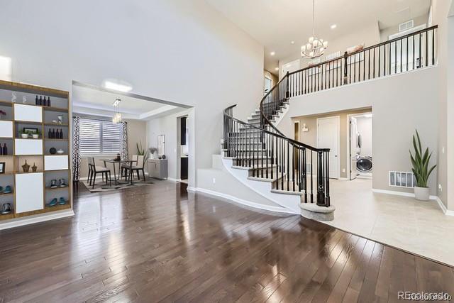 foyer entrance with a notable chandelier, wood-type flooring, a raised ceiling, and a high ceiling