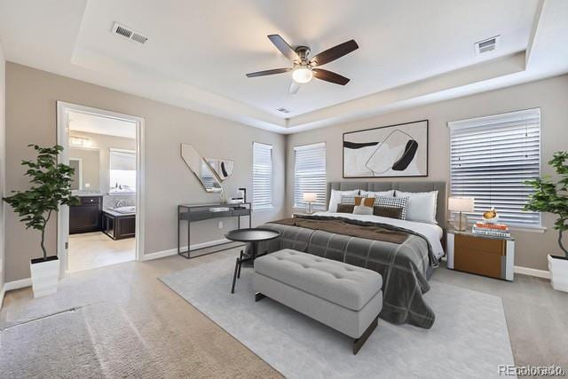 carpeted bedroom featuring ceiling fan, ensuite bathroom, and a tray ceiling