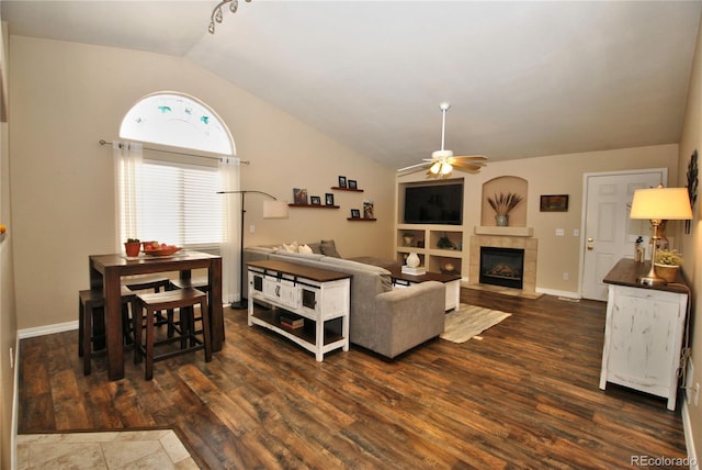 living room with vaulted ceiling, ceiling fan, a tile fireplace, built in features, and dark hardwood / wood-style floors