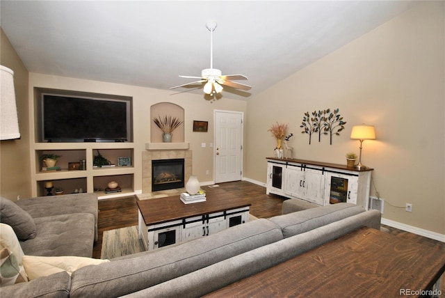 living room featuring ceiling fan, built in features, dark wood-type flooring, and a tiled fireplace