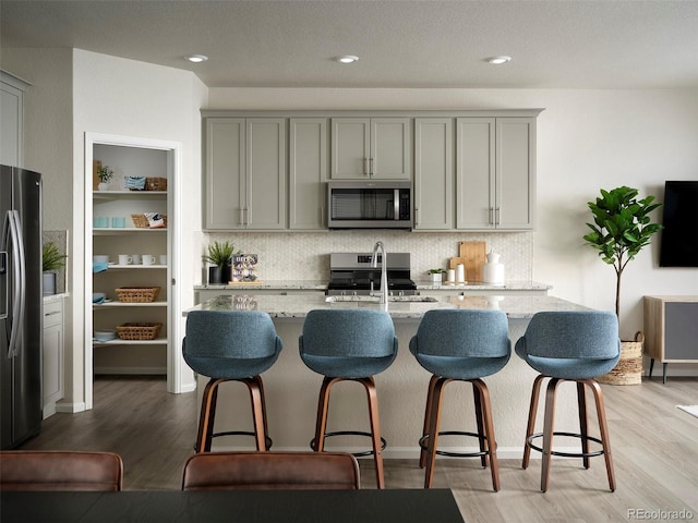 kitchen with light wood-style flooring, light stone counters, gray cabinets, stainless steel appliances, and a sink