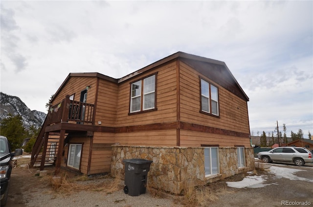 view of home's exterior featuring stone siding, a wooden deck, and stairs