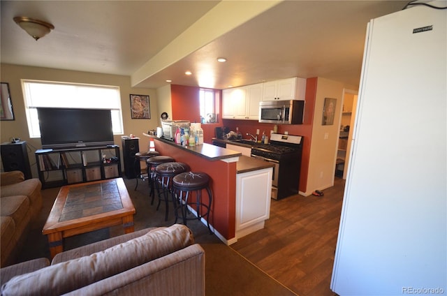 kitchen with a breakfast bar, white cabinets, open floor plan, appliances with stainless steel finishes, and dark countertops