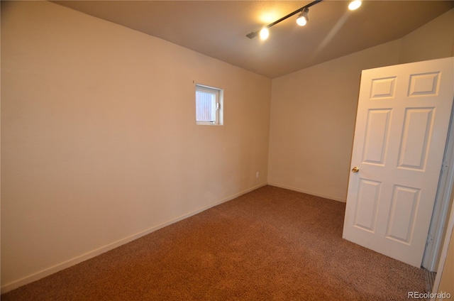 empty room featuring carpet, rail lighting, and baseboards