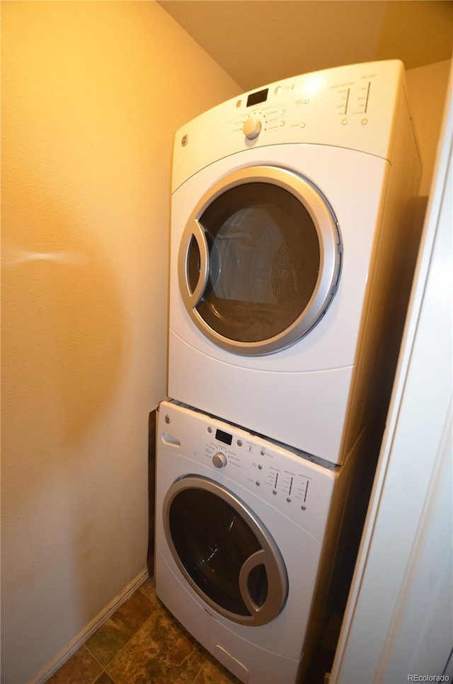 laundry area featuring stacked washer and dryer, baseboards, laundry area, and stone finish flooring