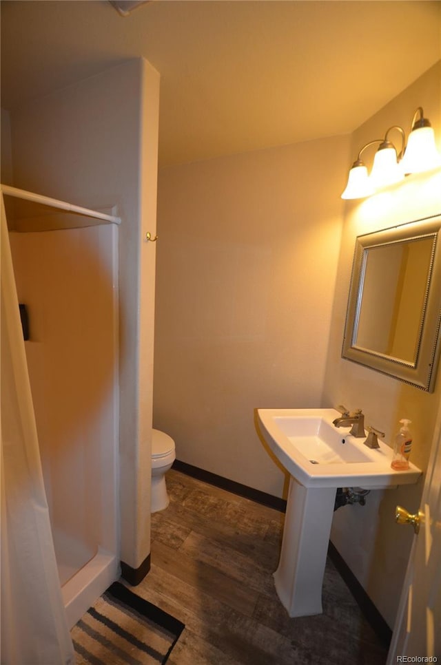 bathroom featuring wood finished floors, a shower stall, toilet, and baseboards