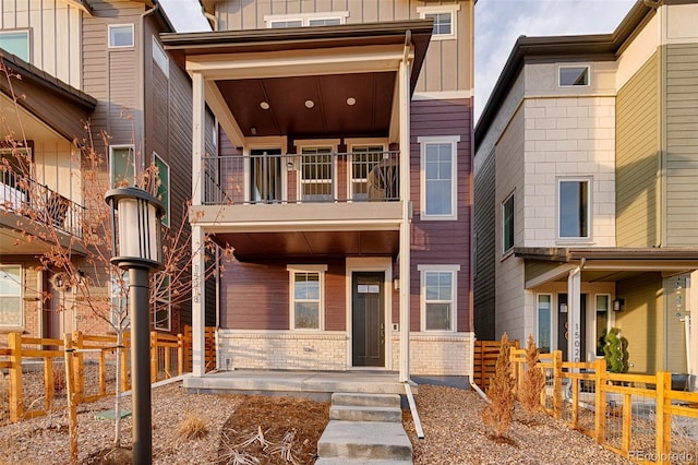 view of front of home featuring fence, a balcony, board and batten siding, and brick siding