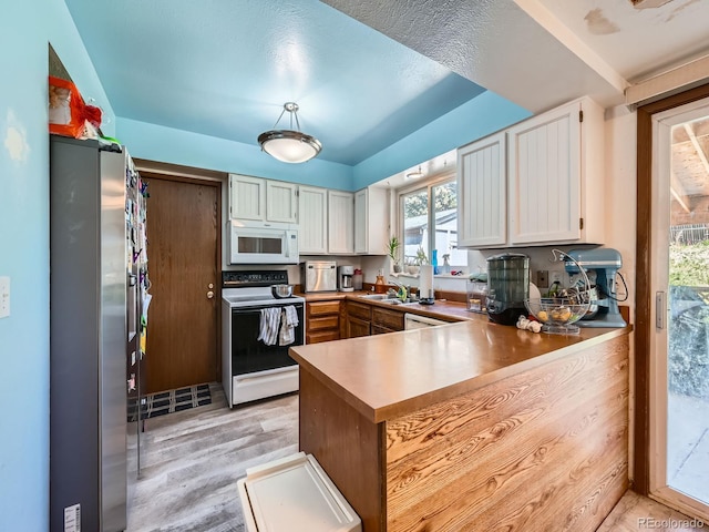 kitchen featuring range with electric cooktop, white microwave, freestanding refrigerator, a peninsula, and light wood-style flooring