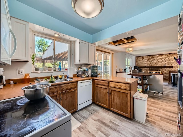 kitchen featuring white appliances, a peninsula, light wood finished floors, brick wall, and brown cabinetry