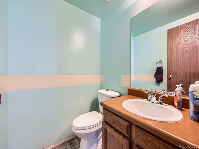 half bathroom featuring toilet, wood finished floors, and vanity