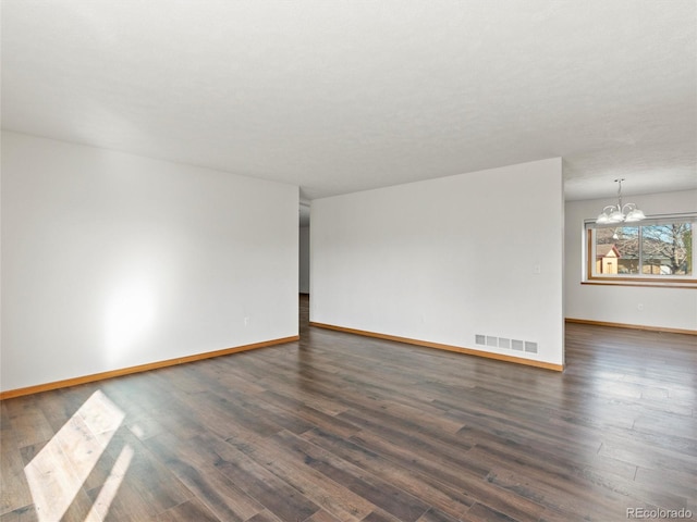 unfurnished room with a notable chandelier and dark wood-type flooring