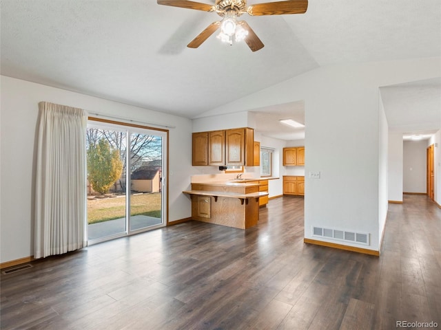 kitchen featuring kitchen peninsula, a kitchen breakfast bar, dark hardwood / wood-style floors, and vaulted ceiling