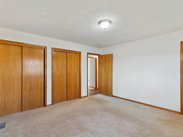 unfurnished bedroom featuring a textured ceiling, light colored carpet, and two closets