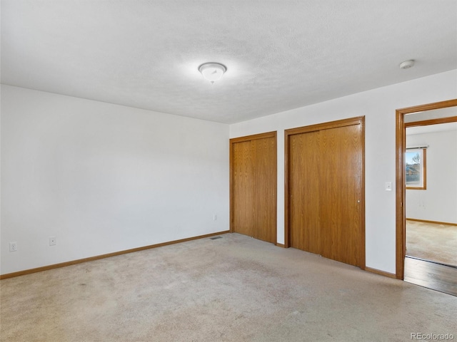 unfurnished bedroom featuring a textured ceiling, light carpet, and two closets