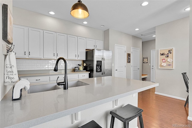 kitchen featuring tasteful backsplash, stainless steel fridge, kitchen peninsula, pendant lighting, and white cabinets