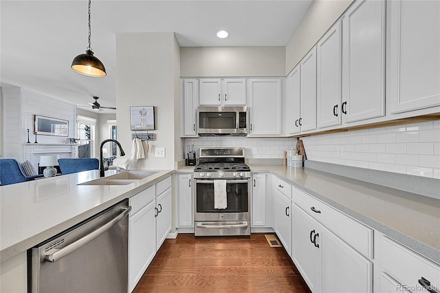 kitchen with dark wood-type flooring, sink, white cabinetry, hanging light fixtures, and stainless steel appliances