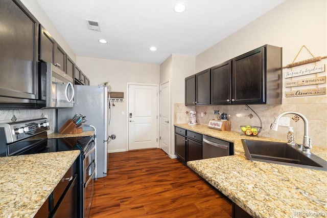 kitchen featuring dark wood-style flooring, light stone countertops, a sink, stainless steel appliances, and decorative backsplash