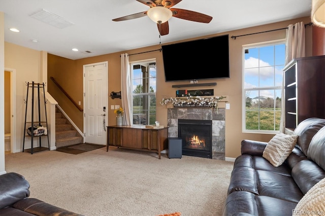 carpeted living area featuring ceiling fan, visible vents, a fireplace, baseboards, and stairs