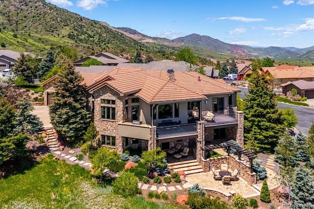 6194 Falcon Ridge Way, Morrison, CO 80465 - back of house with stone siding, a balcony, a tile roof, stucco siding, and a patio