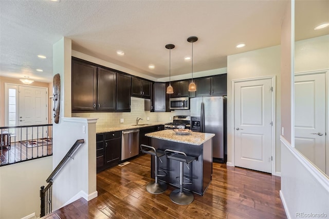 kitchen with pendant lighting, backsplash, appliances with stainless steel finishes, a kitchen island, and light stone counters