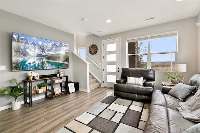 living area with light wood-type flooring, visible vents, baseboards, and stairs