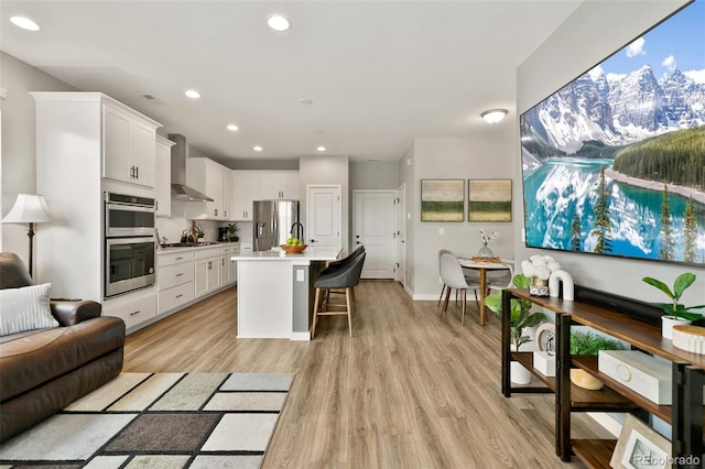 kitchen featuring light wood-type flooring, stainless steel appliances, a breakfast bar, and wall chimney range hood