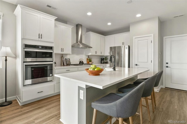 kitchen with visible vents, appliances with stainless steel finishes, wall chimney exhaust hood, and light wood-style flooring