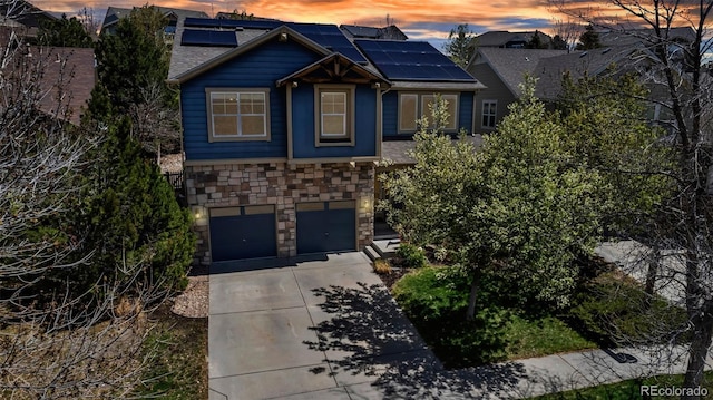 view of front facade with concrete driveway, roof mounted solar panels, stone siding, and a garage
