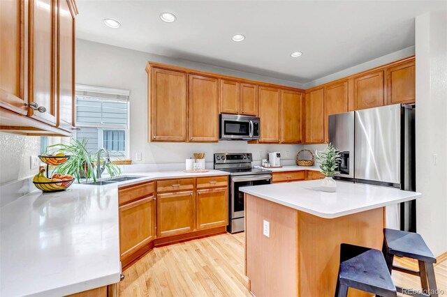 kitchen with a kitchen bar, a sink, light countertops, light wood-style floors, and stainless steel appliances