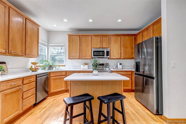 kitchen featuring a breakfast bar, light wood-style floors, light countertops, stainless steel appliances, and a kitchen island