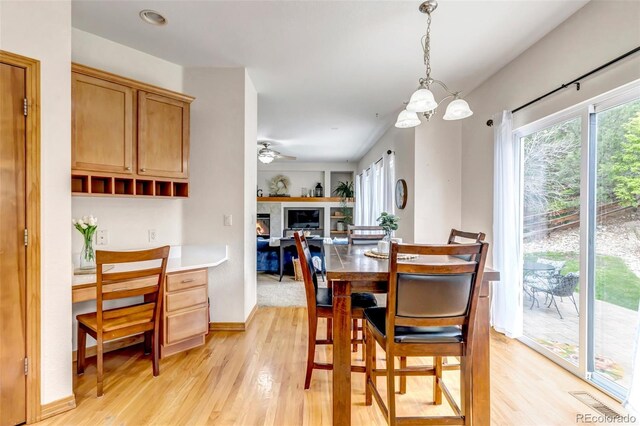 dining space with baseboards, a glass covered fireplace, ceiling fan with notable chandelier, and light wood-style floors