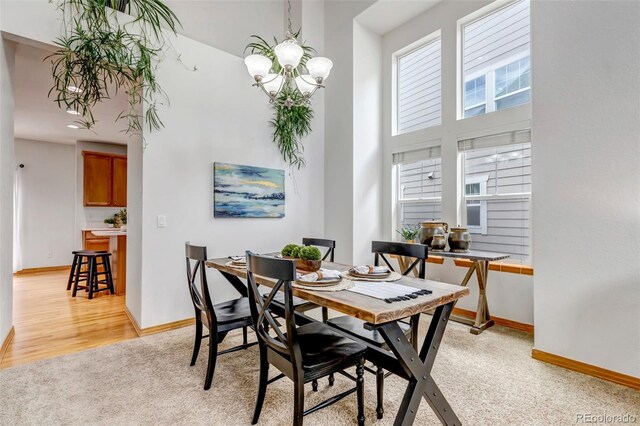 dining space with light colored carpet, baseboards, a notable chandelier, and a high ceiling