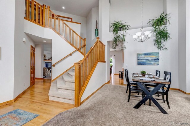dining area featuring a towering ceiling, wood finished floors, baseboards, stairway, and a chandelier