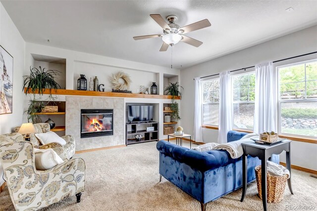 living room with a ceiling fan, built in shelves, a tile fireplace, baseboards, and carpet